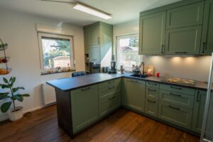 HA-landhauskueche-salbeigruen-u-form-rahmenfront-theke-dunkle-arbeitsplatte